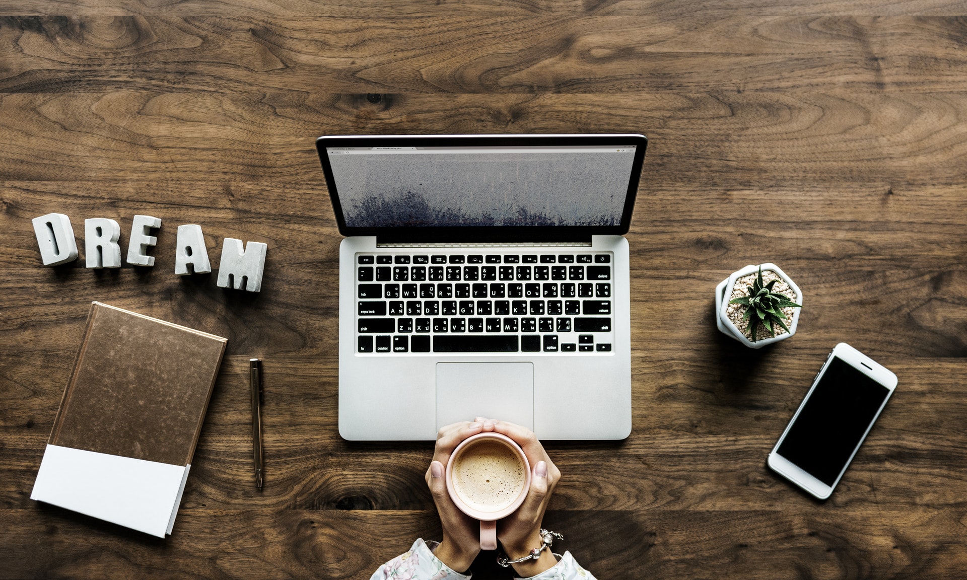 desk with laptop, notebook, pen, hands holding coffee and the word "Dream" in blocks | Purple Horisons Coaching